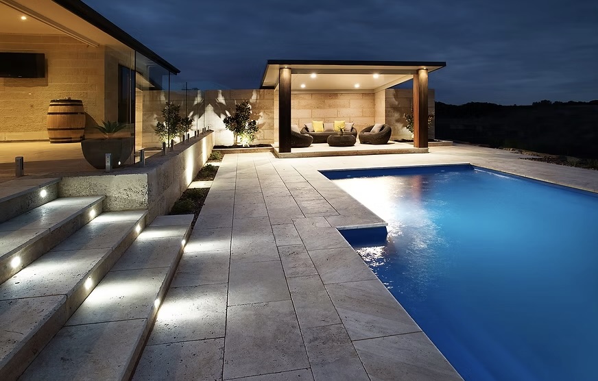 Limestone block paving and steps around a modern poolside entertaining area at dusk